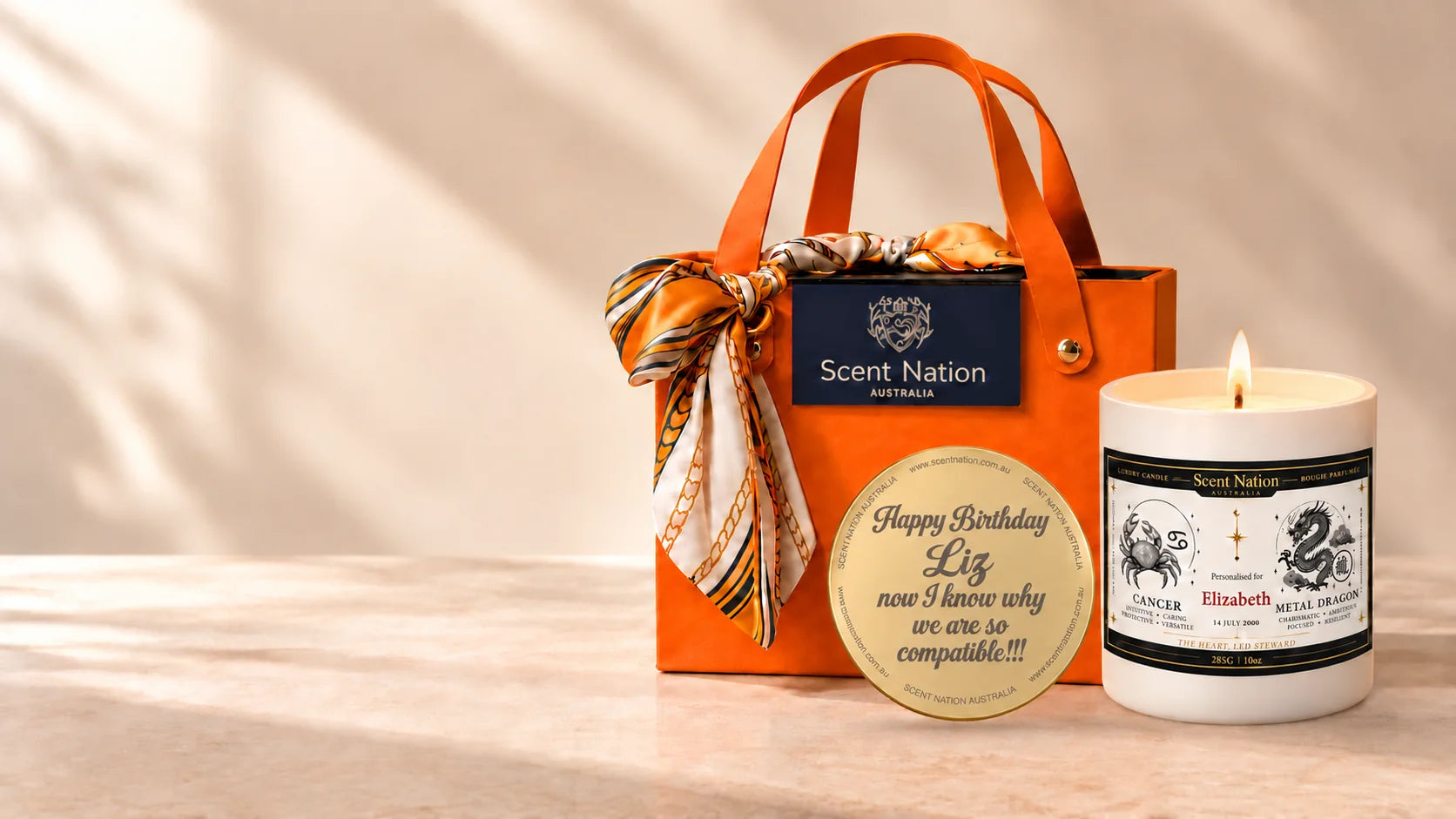 Personalised birthday gift instead of a card – Scent Nation Birthday Story zodiac candle for Elizabeth (Cancer, Metal Dragon) with a gold engraved lid reading Happy Birthday Liz, beside the orange luxury gift bag tied with a silk scarf